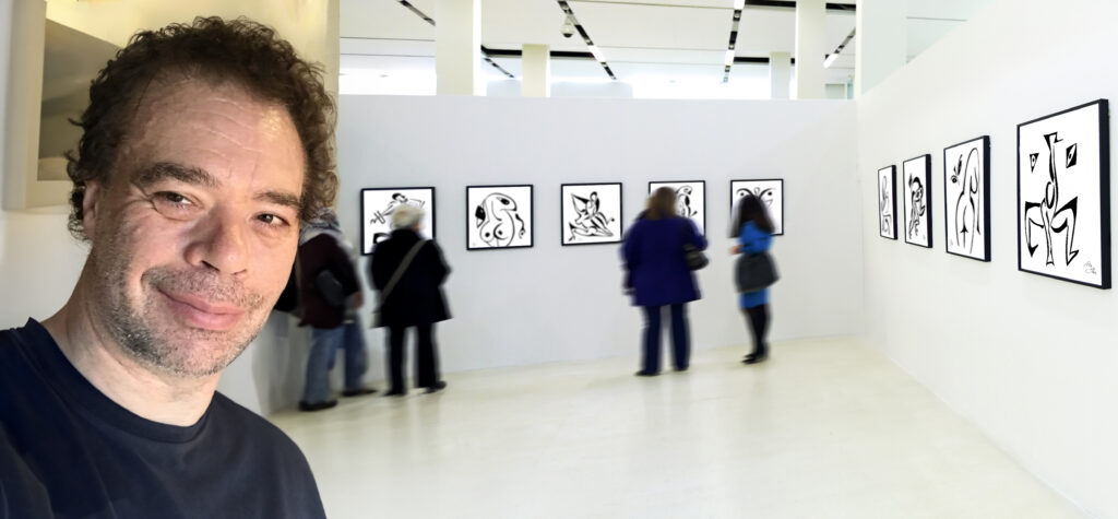 Mikkel Urup smiling in front of his art exhibition, where several black-and-white abstract ink drawings are displayed on a gallery wall.